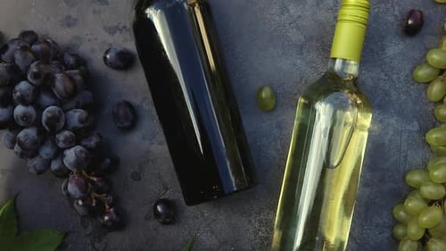 Blick von oben auf Flasche Rot- und Weißwein, grüne Weinrebe, Weinglas und reife Traube auf dunklem Vintage-Stein