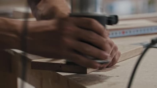 Man in a Carpentry Workshop Working with a Wooden Piece Using a Cutting Instrument