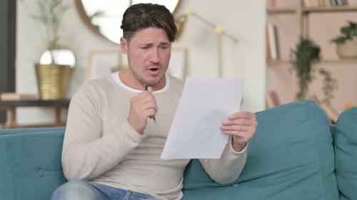 Man Reacts to Paper News While Sitting on Couch