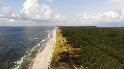 AERIAL: Flying very high over sunny beach while clouds are passing by and cast shadows on the ground