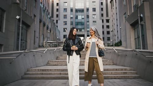 Two Women Walking With Coffee in City