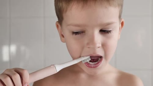 Child Brushing Teeth in Bathroom with Electric Toothbrush