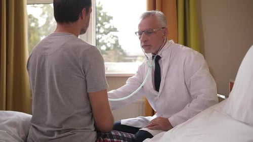 Doctor Using Stethoscope To Examine Patient in Ward