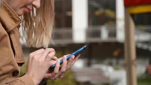 Hands of a Girl on a City Street Are Typing a Message on the Phone