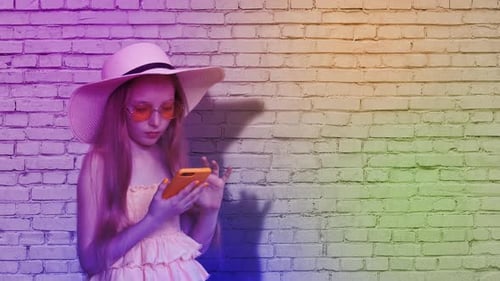 Girl in Sunhat Using Phone by Colorful Brick Wall