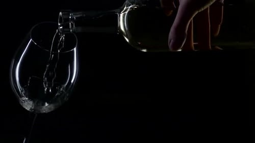 Pouring Clear Liquid into Glass Against Black Background
