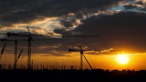 Silhouette of tower crane and large buildings construction site at sunset in evening time.