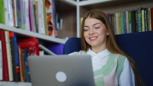 Student, der online studiert und auf dem Laptop in der Bibliothek einen Video-Chat führt