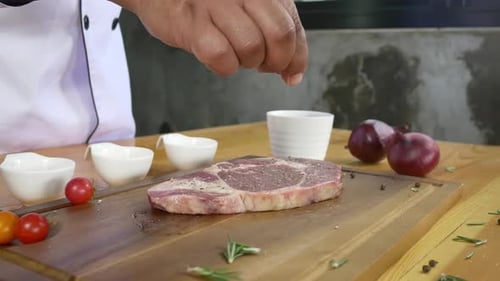 Chef cook season fresh chunk of deli piece of beef with sea salt and grounded spicy peppers.