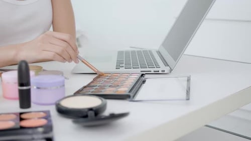 Manos de mujer con aprendizaje de maquillaje con pincel en la mejilla en computadora portátil con curso tutorial.
