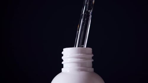 Serum Drops from Dropper into White Bottle