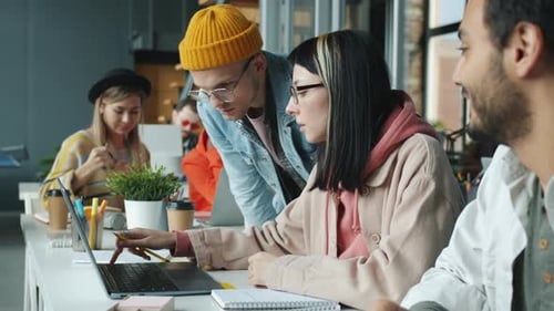 Group of Employees Discussing Business Looking at Laptop Screen Sitting at Desk Indoors in Office
