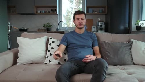 Man Sits On Sofa, Arms Crossed in Apartment