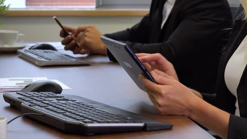 Two office workers, sits at desks in front of computers and work on a tablet and a smartphone