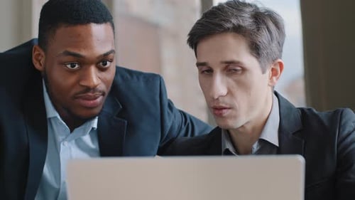 Two Multiethnic Adult Colleagues Looking at Laptop in Office