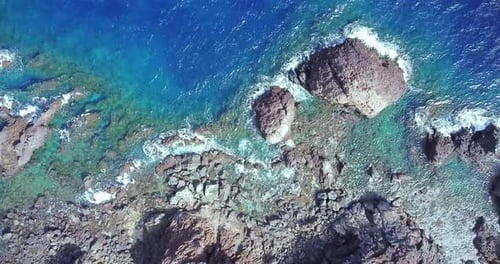 Aerial top view of waves break on rocks in a blue ocean. Sea waves on beautiful beach aerial view