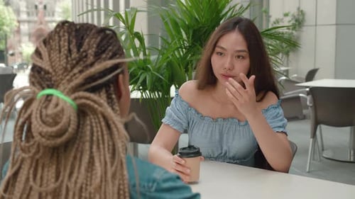 Over the Shoulder Shot of Asian Female Talking Over Coffee Outside a Coffee Shop and Listening