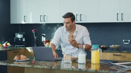 Smiling Man Watching Video Standing in Kitchen. Happy Person Scrolling Computer