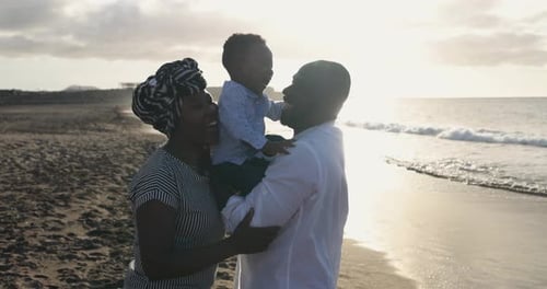 Cheerful african parents enjoy playful moment with little son on the beach outdoor
