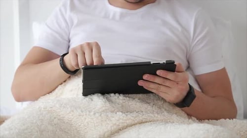 Man Relaxing in Bed Using a Tablet