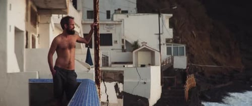 Homem de topless na varanda contemplando o mar