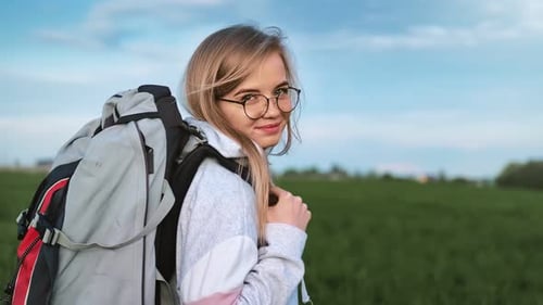Woman with Backpack Walking in a Green Field