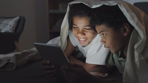 Enfants utilisant la tablette au lit