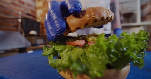 The Cook Hands Placing Top Bun on a Burger. Close Up. Slow Motion