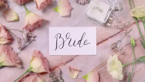 BRIDE card on a marble table near pink flowers top view zoom in