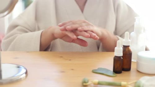 Woman Applies Lotion to Hands at Vanity