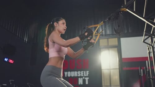 Asian young athlete woman doing cardio exercise and squatting with rope system in fitness gym.