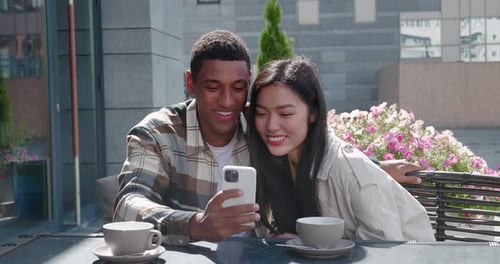Young Multiracial Loving Couple Sitting Together in the Outdoor Cafe on Beautiful Sunny Day at
