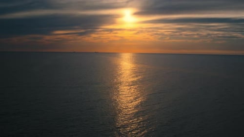 Meeresoberfläche vor friedlichem bewölktem Himmel mit gelber Sonne