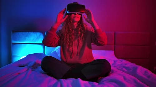 Junges Mädchen sitzt nachts auf dem Bett und benutzt Virtual-Reality-Headset