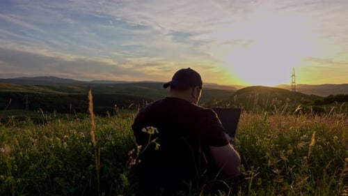 Man Working on Laptop at Sunset in Field