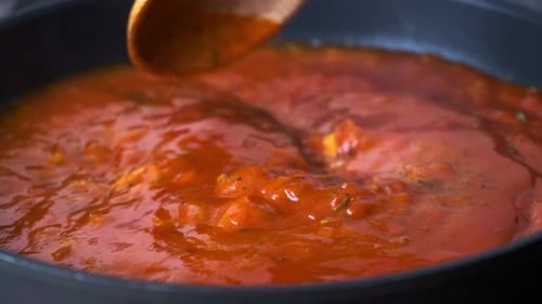 Cooking tomato sauce in black frying pan, close up.