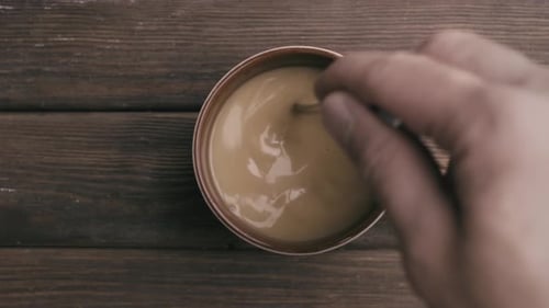 Hand Stirs Creamy Coffee in Mug on Wood Table