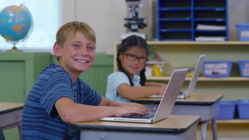 Portrait of two kids in school classroom with laptop computers