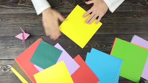 Hands Folding Yellow Origami Paper on Table
