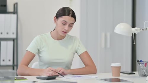 Woman Calculates Finances at Desk in Office