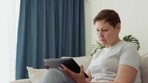 Woman Using Tablet Device on Couch Indoors