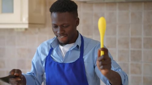 Joyful Male African American Cook in Apron Looking at Camera Imitating Fighting with Cooking