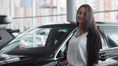 Happy Woman Posing beside New Car in Auto Showroom