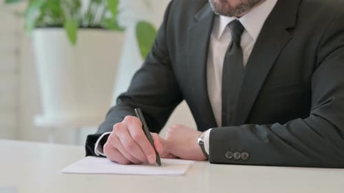 Close Up of Middle Aged Businessman Writing on Paper with Pen
