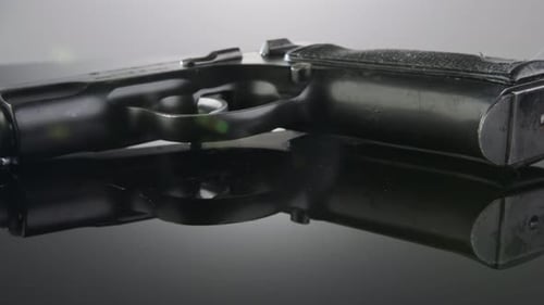 Waffenkontrolle. Studioaufnahme einer 9-mm-Pistole, die sich auf einer reflektierenden Oberfläche dreht
