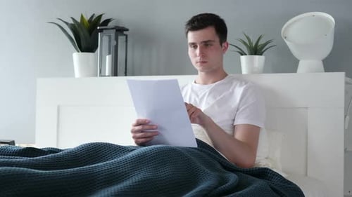 Young Man Reading Paperwork in Bed