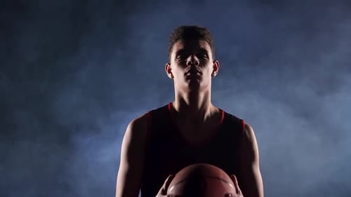 Porträt eines jungen afroamerikanischen Basketballspielers in einem dunklen, rauchigen Studio im Rampenlicht