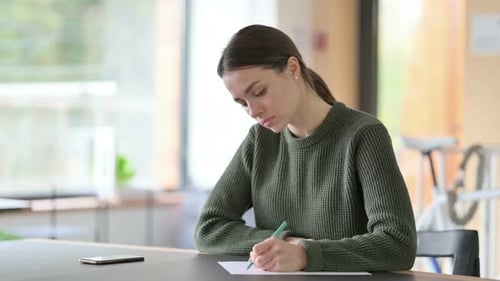 Focused Young Woman Writes on Paper at Desk