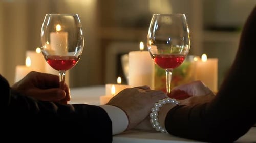 Romantic Couple Holds Hands Over Wine and Candlelight