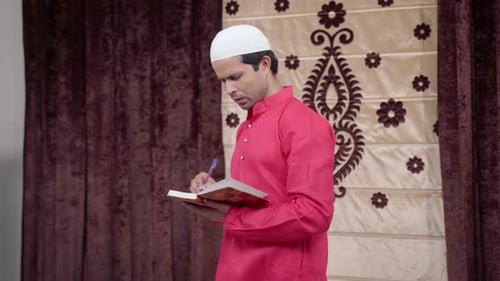 Man Writes Notes in Religious Book Indoors